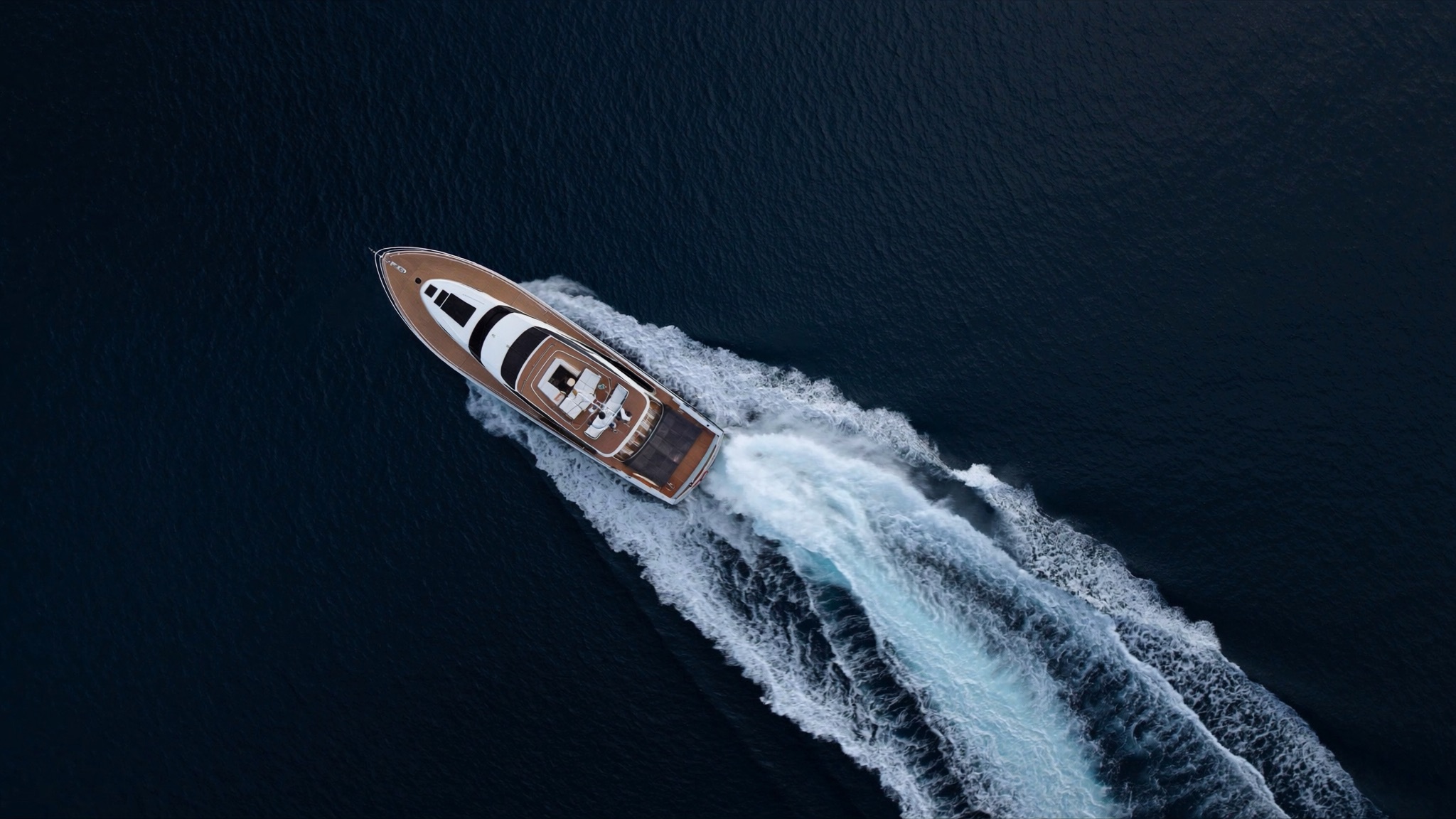 Yacht visto dall'alto che taglia il mare blu scuro lasciando una lunga scia bianca